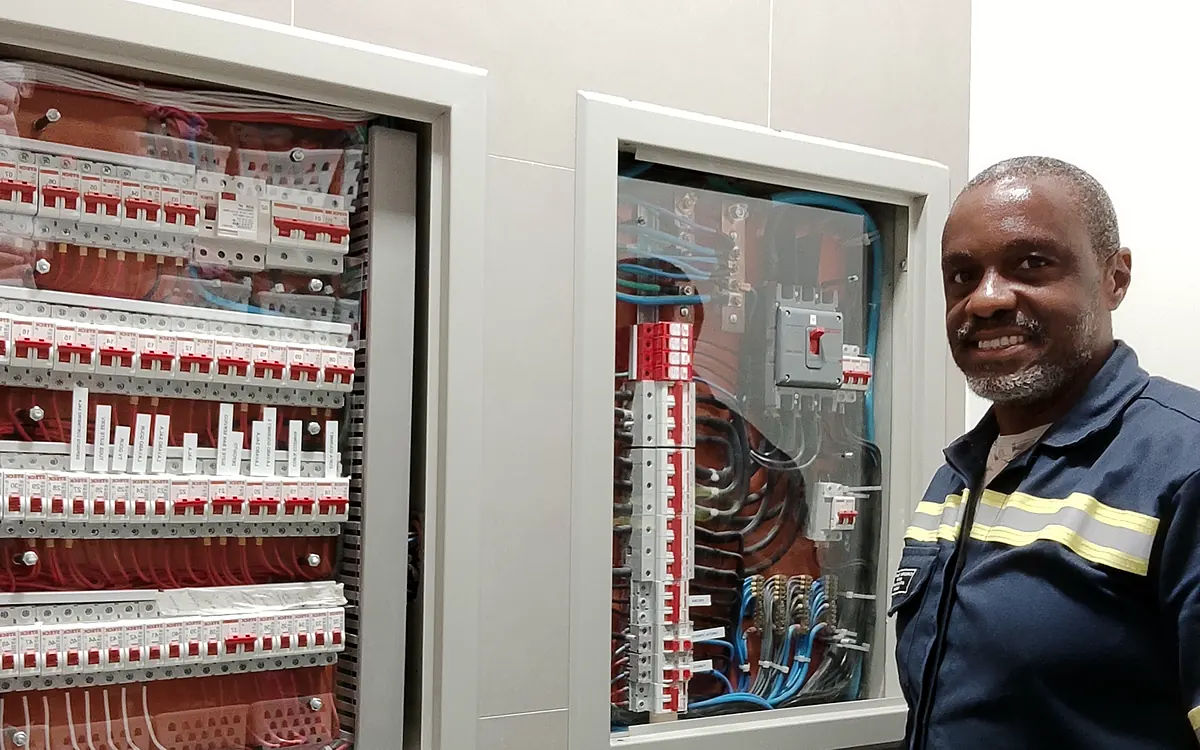 Eletricista Ronaldo Américo ao lado de quadros de distribuição organizados conforme a NBR 5410
